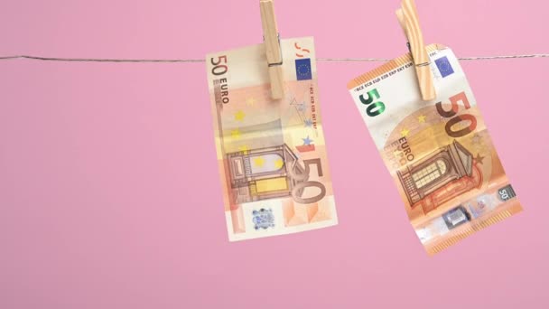 roikkuu pyykkinarulla rahaa Euroopan unionin 50 euroa, vaaleanpunainen tausta. Rahanpesun käsite, hyöty - Materiaali, video