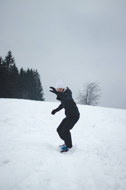 Ein sechzehnjähriger Junge fährt auf einem blauen Snowboard aus Plastik. Der Teenager versucht, sein Gleichgewicht auf dem Brett zu halten. Reiten Sie auf einem instabilen Brett. Sie probieren Neues aus. Wintersport. Skifahren im Dorf. Lächelnder Junge. - Foto, Bild