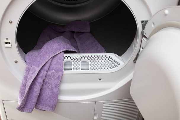 Modern bir çamaşır kurutma makinesinin açık kapısı. İçeride kuru bir havlu var.. - Fotoğraf, Görsel