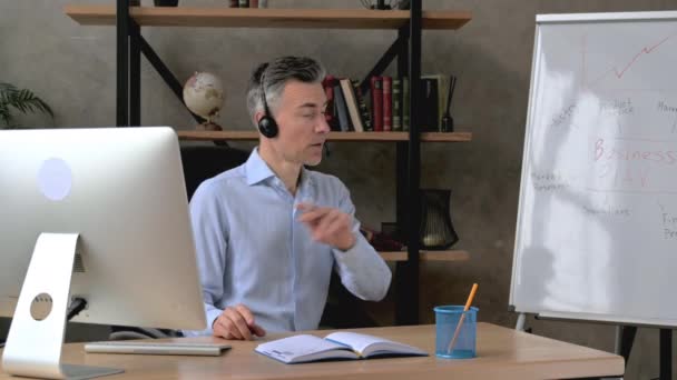 Serious influential intelligent caucasian middle aged ceo, manager or business mentor, conducts online briefing for coworkers via video conference, shows a presentation, business plan on a flipchart - Footage, Video
