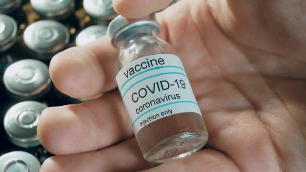 Mies, jolla on koronavirusrokote pullossa farmakologisissa lääkkeissä injektiopulloissa taustalla maailmanlaajuista pandemiaa vastaan - Materiaali, video