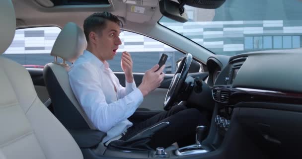 Impresionado hombre de negocios asustado por un mal mensaje en su teléfono inteligente, sentado en el asiento del conductor en el coche. Concepto de quiebra - Imágenes, Vídeo