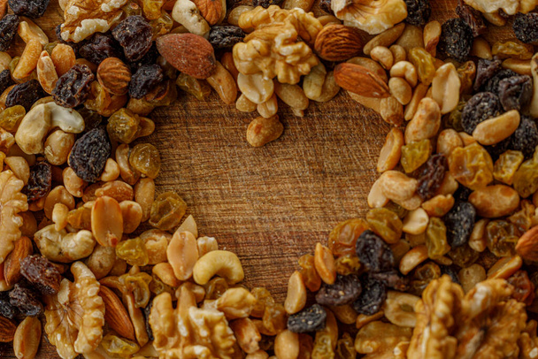 A macro photography of mix nuts. Raisins and a variety of dried fruits, grouped together forming a heart on a wood texture. Almonds, walnuts, hazelnuts, cashew, peanuts. - Photo, Image