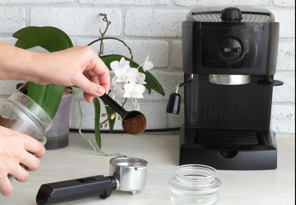На кухонному столі стоїть чорна кавоварка. Рука вливає мелену каву в ріг. Концепція приготування домашньої кави. Горизонтальна орієнтація
.  - Фото, зображення