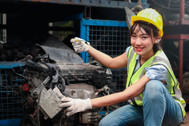 Industrial smiling woman worker wearing helmet repairing with machinery at manufacturing plant factory industry, Asian beautiful female engineer and many engine parts as blurred background - Photo, Image