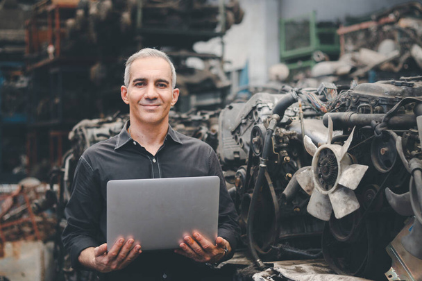 Brygadzista przemysłowy korzystający z laptopa w fabryce zakładów produkcyjnych, starszy inżynier męski z wieloma częściami silnika jako niewyraźne tło - Zdjęcie, obraz