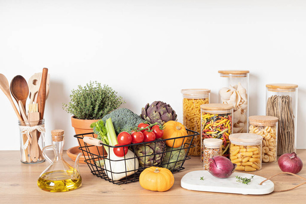Assortment of pasta in glass jars, olive oil, vegetables and kitchen utensils on wooden table. Traditional italian ingredients, healthy balanced food, sustainable lifestyle, zero waste eco friendly concept. - Photo, Image