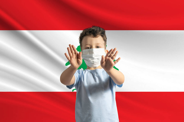 Μικρό λευκό αγόρι με προστατευτική μάσκα στο φόντο της σημαίας του Λιβάνου. Κάνει στοπ με τα χέρια του, μένει στο σπίτι Λίβανος. - Φωτογραφία, εικόνα