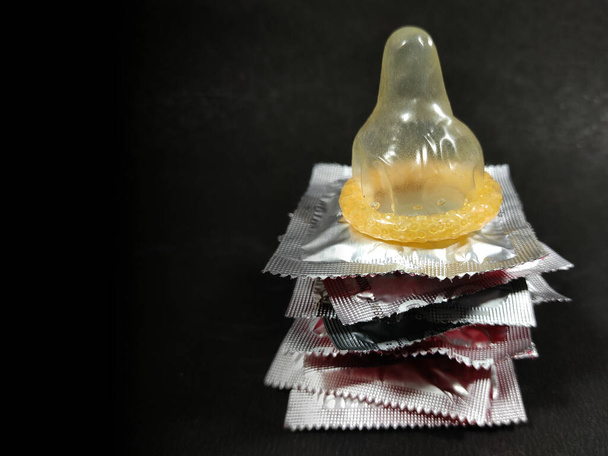 Αρσενικό αντισυλληπτικό μέθοδος Condom διατηρούνται σε πακέτα σε μαύρο φόντο με χώρο για κείμενο. - Φωτογραφία, εικόνα