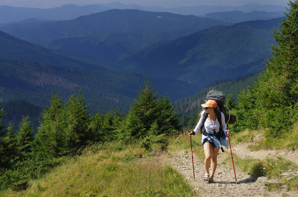 Женщина-туристка с рюкзаком, взбирающаяся на склон горы. Туристический отдых. Национальный день прогулок 17 ноября - Фото, изображение