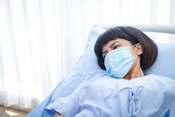 Uma paciente usando máscara está deitada em uma cama de hospital. Tratamento de pacientes durante a epidemia de coronavírus. Conceito de serviço médico. Espaço de cópia - Foto, Imagem