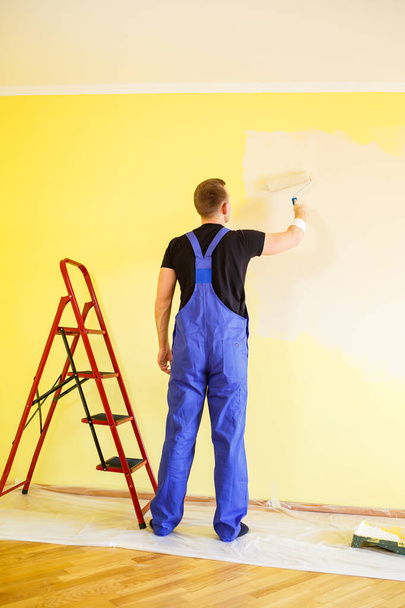 Αρσενικό ειδικός χρωματίζει τον τοίχο με χρώμα σε εσωτερικούς χώρους, επισκευή έννοια - Φωτογραφία, εικόνα