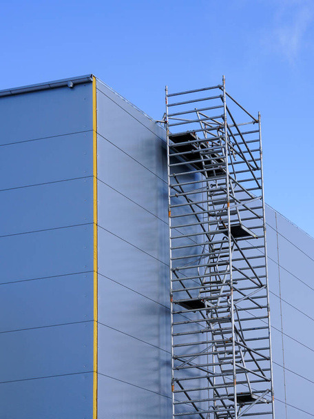 edificio de fábrica de marco de metal inacabado, cubierto con paneles sándwich grises contra un cielo azul - Foto, Imagen