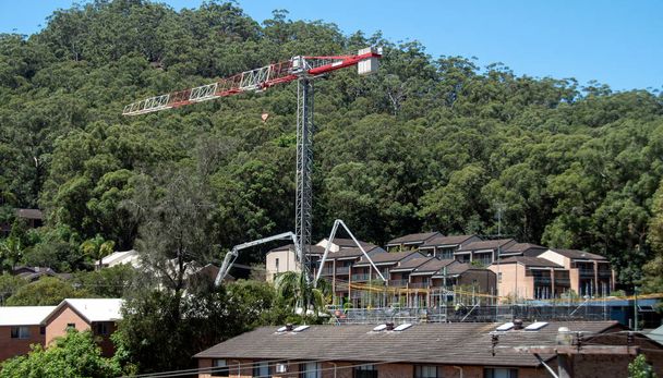 コンクリートブームポンプは、ブッシュランドの背景を持つ新しい建物のサイトに材料を提供します。56-58ビーンセントゴスフォードで新しい社会住宅住宅の住宅ユニットの開発。2021年2月26日。シリーズ風景画の一部。オーストラリア. - 写真・画像