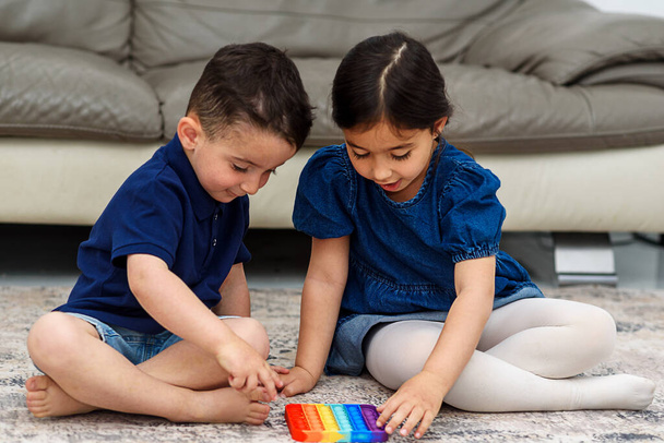 Два симпатичных малыша играют с гибкой игрушкой Pop It fixed. - Фото, изображение