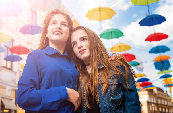 Dvě krásné mladé dívky procházející se po městě. Barevné deštníky na obloze. - Fotografie, Obrázek