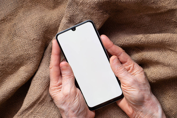 phone with a white screen in the hands of an elderly woman on the table close-up, white screen on the phone - Photo, Image