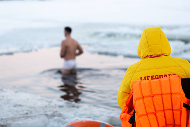 Рятувальники спостерігають за людьми, які занурюються в льодову діру. Люди купаються в крижаній воді
 - Фото, зображення