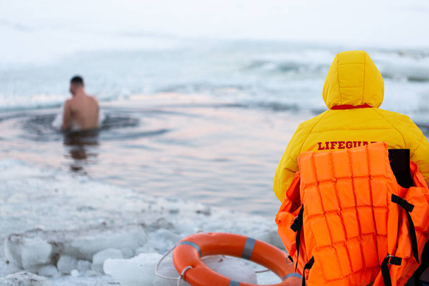Redders kijken naar mensen die in een ijsgat duiken. Mensen baden in ijskoud water - Foto, afbeelding