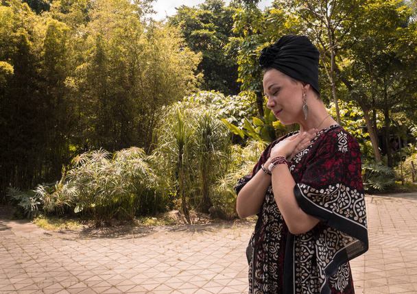 Biała kobieta z czarnym turbanem o zrelaksowanej twarzy i z rękami na sercu - Zdjęcie, obraz
