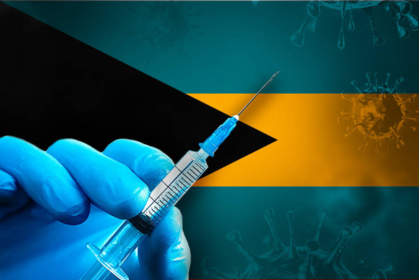 Εκστρατεία Εμβολιασμού Μπαχάμες Covid-19. Ένα χέρι σε ένα μπλε λαστιχένιο γάντι κρατά μια σύριγγα με εμβόλιο ιού covid-19 μπροστά από τη σημαία των Μπαχαμών. Έννοια εμβολιασμού κατά του ιού του κερατοειδούς - Φωτογραφία, εικόνα