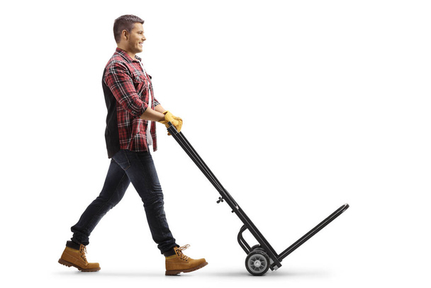 Full length profile shot of a man pushing an empty hand truck isolated on white background - Foto, Imagem