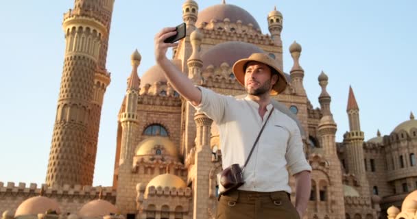 un hombre con un sombrero de viaje y camisa de lino con un teléfono, tomar selfie - Imágenes, Vídeo