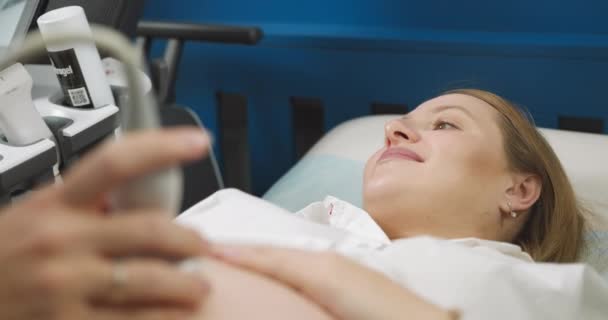 Закрыть руки врачей, используя современное ультразвуковое оборудование для скрининга живота беременной женщины. Счастливая беременная женщина ложится на УЗИ. - Кадры, видео