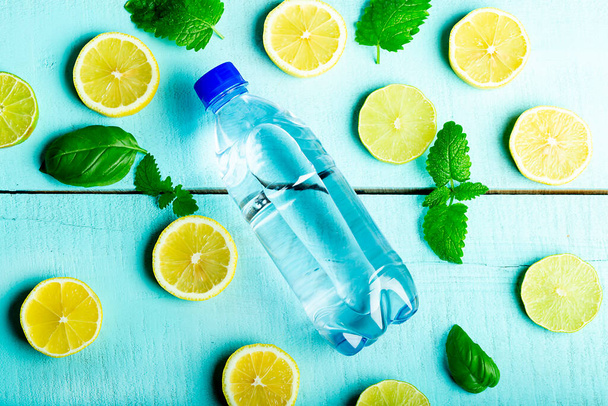 Een fles zuiver water, liggend op een houten turquoise ondergrond met citroenen, munt en ijs, close-up - Foto, afbeelding