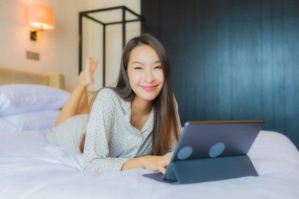 Портрет красива молода азіатка використовує планшет з кредитною карткою на ліжку в інтер'єрі спальні
 - Фото, зображення