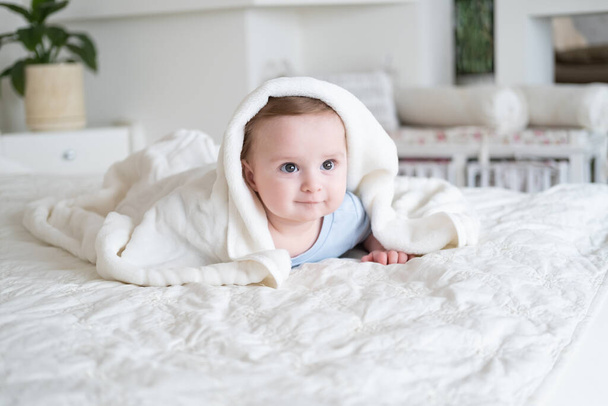 niedliche Baby Junge 6 Monate alt in blu Body lächelnd und liegend auf dem Bett mit weißem Karo zu Hause - Foto, Bild