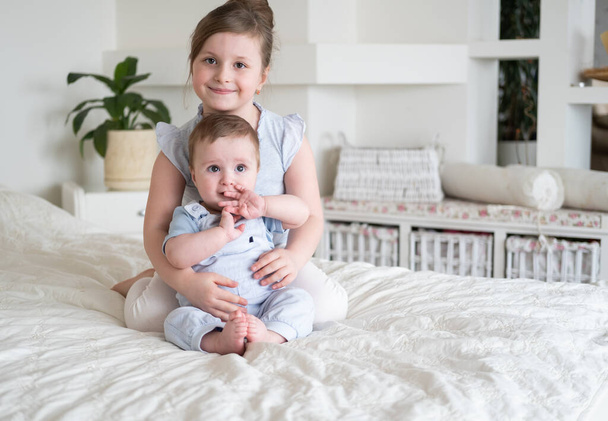 cute little girl older sister with her baby boy brother at home sitting on bed. - Φωτογραφία, εικόνα