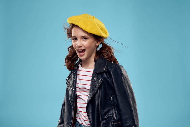 Fashionable girl in a yellow beret and leather jacket striped T-shirt blue background - Foto, Imagem
