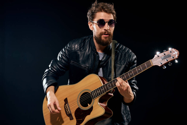férfi egy gitár a kezében fekete bőr kabát napszemüveg zene érzelmek fekete háttér - Fotó, kép