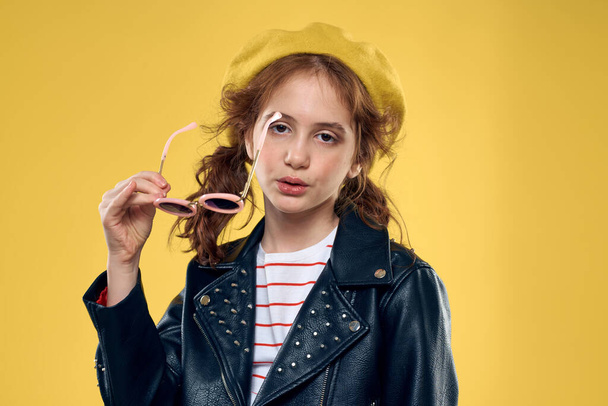 Wesoła dziewczynka w okularach przeciwsłonecznych i kapelusz styl życia studio żółty tło moda - Zdjęcie, obraz