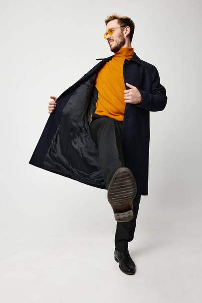mignon gars dans un pull orange manteau déboutonné pantalon modèle fond clair - Photo, image