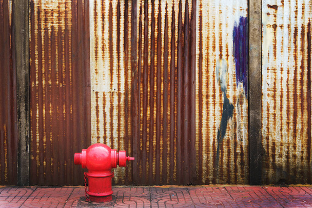 錆びた段ボール鉄金属フェンスの上を歩く赤い消火栓コピースペースのある亜鉛の壁の背景 - 写真・画像