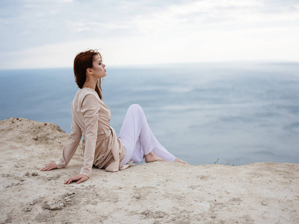 Una donna in natura in abiti leggeri siede sulla sabbia e l'oceano sullo sfondo - Foto, immagini