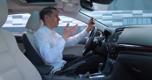 Молодий бізнесмен має відеочат за допомогою смартфона, сидячи в машині. Чоловічий водій розмовляє відеодзвінком на мобільному телефоні
. - Кадри, відео