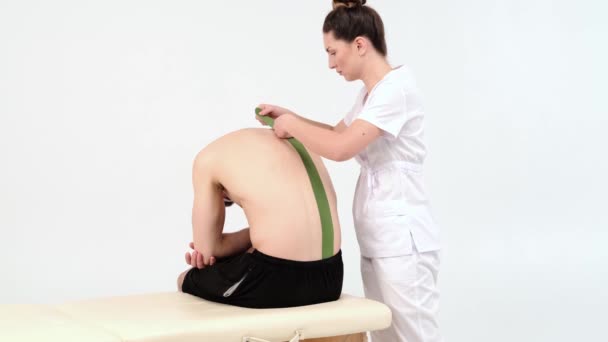 Physiotherapeut klebt Kinesiobänder auf den Rücken des Patienten, Kinesiologie-Taping, Kinesiologische Therapie, Sportler erholen sich nach Lendenverletzung, 4k - Filmmaterial, Video