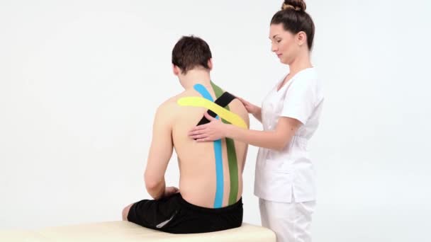 Fysioterapeutti tarttuu kinesio-nauhoihin potilaan selkään, kinesiologiseen teippaukseen, kinesiologiseen hoitoon, urheilija toipuu kupeiden loukkaantumisen jälkeen, 4k - Materiaali, video