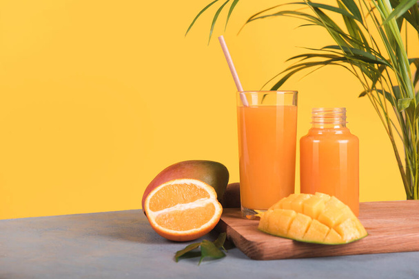 Glas vers sinaasappel- en mangosap en schijfje sinaasappelfruit op gele ondergrond - Foto, afbeelding