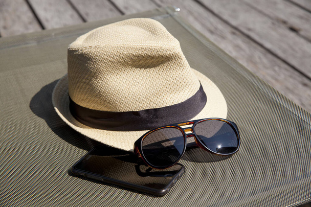 Primer plano de sombrero de paja y gafas de sol en sofá cama junto a la piscina. Vacaciones en concepto de vacaciones de verano. - Foto, imagen