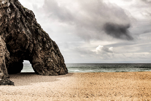 シントラ、リスボン、ポルトガルのアドラガのビーチで勇敢な海、岩の形成と曇りのドラマの空 - 写真・画像