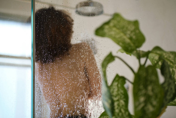 Rückansicht. Die defokussierte Frau badet in der Duschkabine, fühlt sich entspannt und sauber, vergisst ihren Alltag. Menschen, Lebensstil und Erfrischungskonzept - Foto, Bild