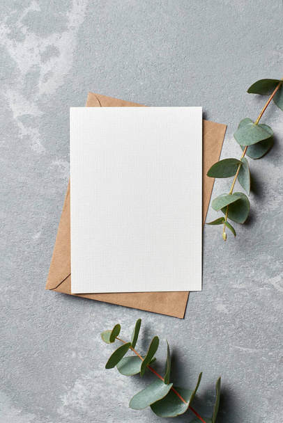 Greeting card mockup with envelope and eucalyptus twigs on grey concrete background - Foto, afbeelding