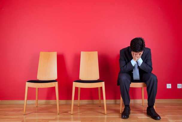 Sad businessman sited next to a red wall - 写真・画像