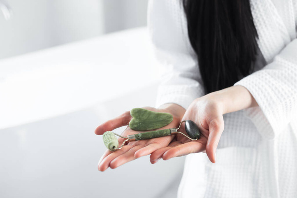 Rouleau vert jade et grattoir de massage gua sha dans les mains de la femme - Photo, image