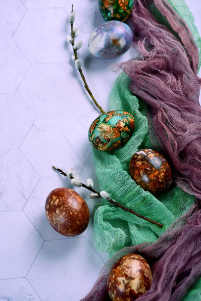 緑と茶色のガーゼの布と柳の枝で飾られた光の背景に自然に描かれたイースターの卵、自然素材でイースターの卵の着色、スペースをコピー  - 写真・画像