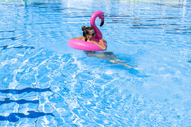 Piscina de mujeres jóvenes. Chica sexy joven feliz en traje de baño bikini, gafas de sol con flotador de flamenco inflable rosa en agua azul. Vacaciones de viaje. Belleza, bienestar, estilo de vida - Foto, Imagen